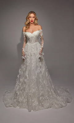 A woman stands in the Long White Dress: Alyce 7150, an off-the-shoulder, long-sleeved gown with lace and ruffle details and a flowing train, elegantly draped against a plain backdrop.
