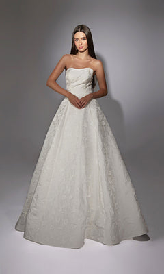 A woman stands against a plain background wearing the Alyce 7155 Long White Dress—a strapless, floor-length gown with a full skirt and subtle floral jacquard fabric.