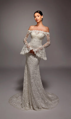 A woman stands in a studio with a neutral background, wearing the Long White Dress: Alyce 7156—an off-shoulder bridal gown featuring long lace sleeves.