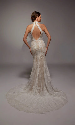A woman wears the Alyce 7159 long white dress, featuring an ivory mermaid silhouette, lace halter-neck, open back, and long scalloped train, standing against a plain gray background.