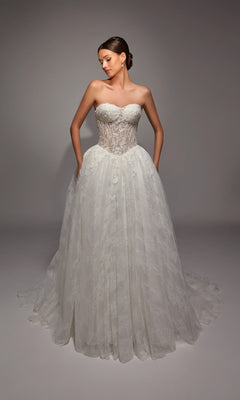 A woman poses in the Alyce 7163, a long white dress with an ivory strapless corset bodice and full lace skirt, hands in pockets, against a plain studio background.