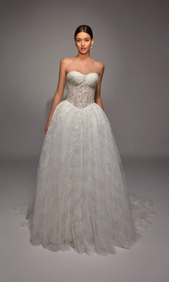 A woman poses in the Long White Dress: Alyce 7163, featuring a strapless, sheer corset bodice and full lace skirt, set against a plain studio backdrop.