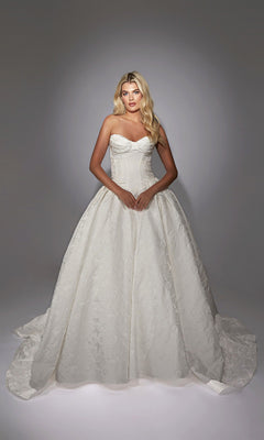 A woman stands against a plain gradient background wearing the Long White Dress: Alyce 7164, a strapless white ball gown with a fitted bodice, full skirt, and elegant floral jacquard fabric for luxurious texture and style.