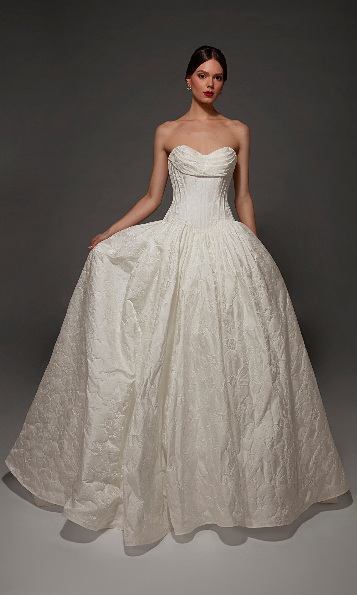 A woman stands against a dark background wearing the Long Wedding Dress: Alyce 7165 in Diamond White, featuring a strapless sweetheart neckline, textured fitted bodice, and a full jacquard skirt.