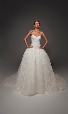A woman poses with her hands on her hips against a dark background, wearing the Alyce 7169 long wedding dress in diamond white, which features a sweetheart neckline, fitted bodice, and a full lace skirt.