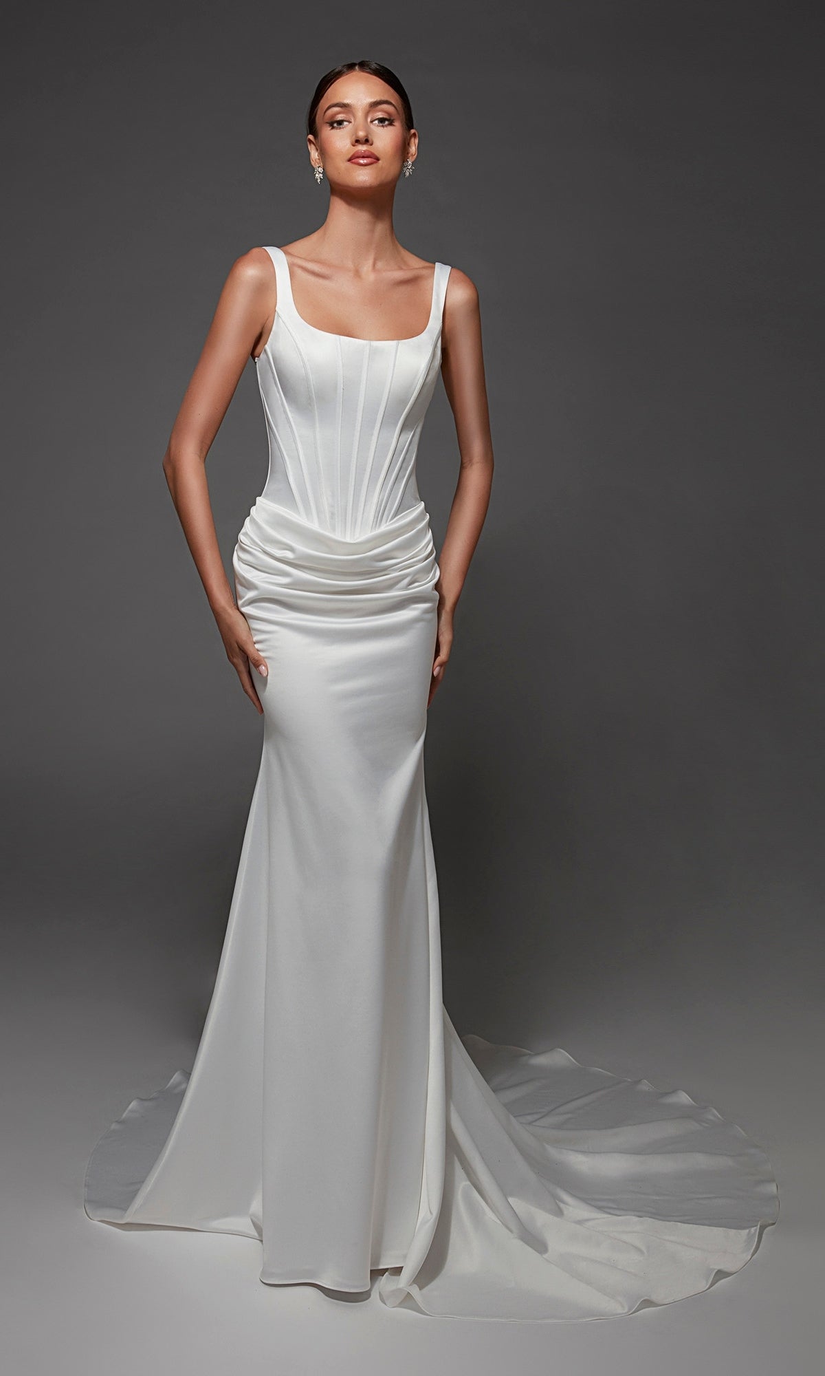 A woman wearing the Alyce 7171 long wedding dress in Diamond White, a fitted sleeveless satin gown with a square neckline, structured boned corset bodice, and subtle train, stands against a plain dark background.