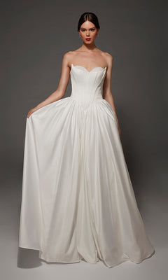 A woman wearing the Long Wedding Dress: Alyce 7172 in Diamond White, featuring a strapless sweetheart neckline, fitted bodice, and full skirt, stands against a plain gray background.