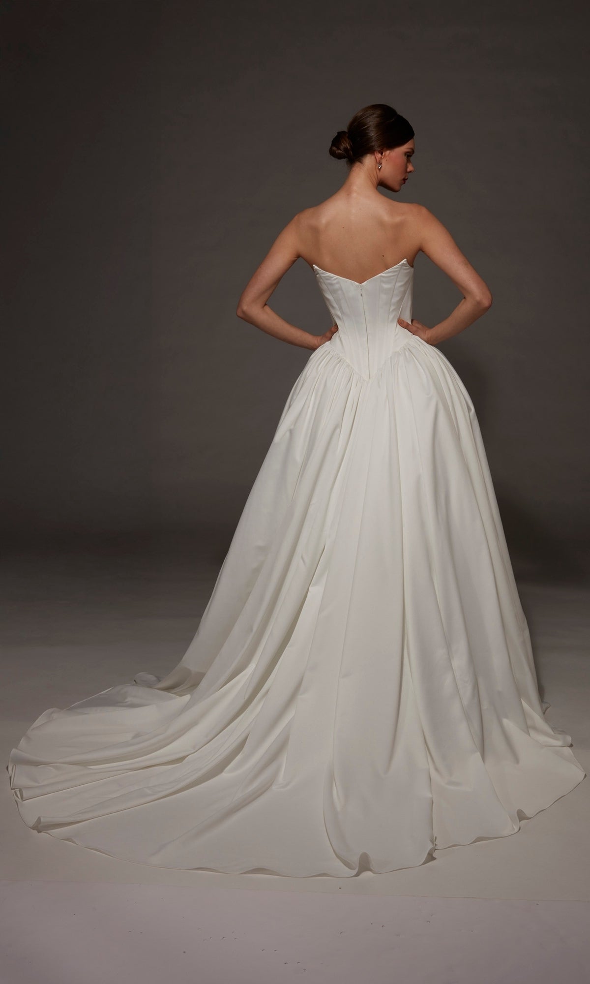 A woman stands with her back to the camera, wearing the Alyce 7172 long wedding dress, featuring a strapless sweetheart neckline, satin ball gown silhouette, and a long, flowing train.