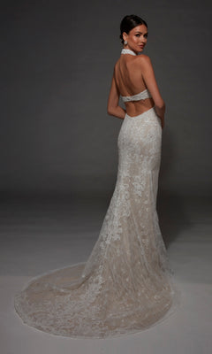 A woman poses against a dark background wearing the Alyce 7173 long wedding dress, featuring a backless design, halter straps, lace detailing, and a flowing train.