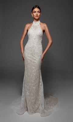 A woman wearing the Long Wedding Dress: Alyce 7173, a sleeveless, high-neck lace gown with a fitted bodice, subtle train, and elegant halter strap detail, stands against a plain gray background.