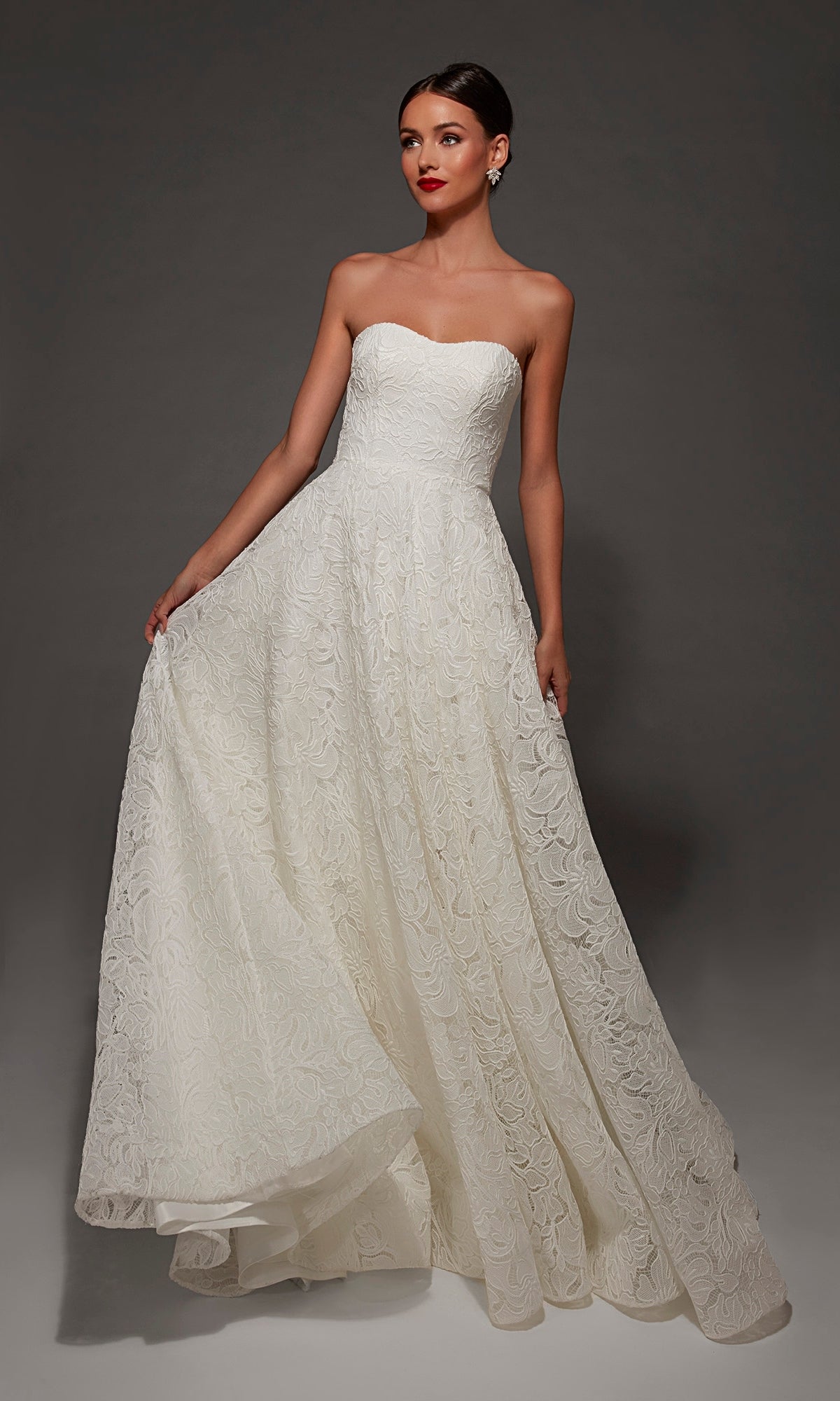 A woman poses elegantly against a dark gray background, wearing the Alyce 7178 long wedding dress in Diamond White, featuring a strapless sweetheart neckline, full-length white lace design, and a graceful chapel train.