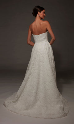 A woman faces away, showcasing the Long Wedding Dress: Alyce 7178—a strapless gown with a sweetheart neckline, floral textured pattern, fitted bodice, and a long, flowing chapel train—standing against a dark background.