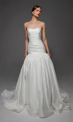 A woman stands against a plain gray background wearing the Alyce 7181 long wedding dress, which features a strapless satin design with a fitted bodice and a full, flared mermaid skirt.