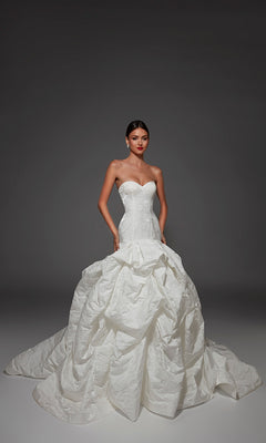 A model wears the Alyce 7185 long wedding dress, featuring a stunning strapless sweetheart neckline, a fitted corset bodice, and a voluminous ruffled ball-gown skirt that flows into a dramatic long train.
