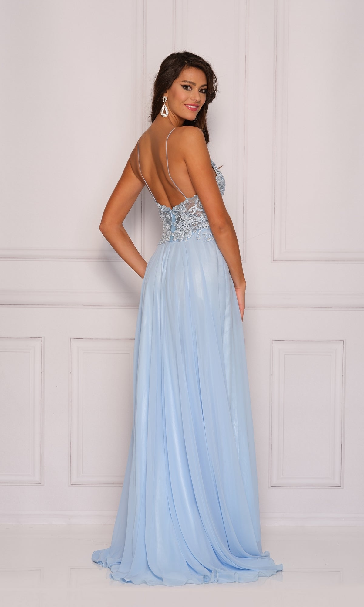 Woman in a light blue Classic Long A-Line Prom Gown (Dave & Johnny A7248) with an embroidered lace bodice and thin straps, standing sideways and smiling against a white paneled wall.