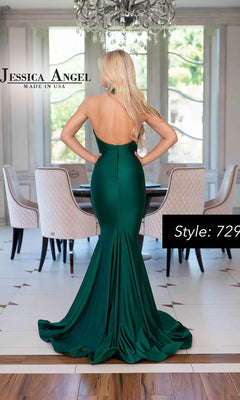 A woman with long blonde hair models the Jessica Angel 729, a fitted emerald green halter mermaid formal dress, standing with her back to the camera in a modern dining room.