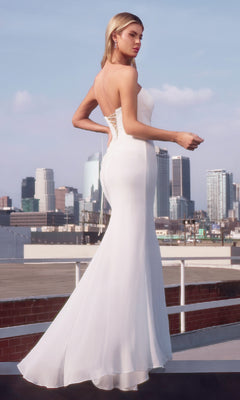 A woman in the affordable Ladivine 7434W—a strapless, form-fitting long white prom dress—stands on a rooftop with the city skyline behind her.