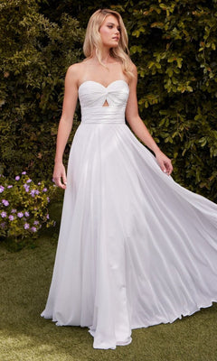 A woman wears the Strapless Long White Prom Gown: Ladivine 7435W, featuring a sweetheart bodice and small front cutout, as she stands outdoors on grass near green bushes and purple flowers.