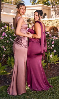 Two women, each wearing the Long Prom Dress: Ladivine 7437—one in rose gold and the other in deep magenta—stand side by side in a lush garden surrounded by flowers and greenery, facing the camera. The elegant satin prom dresses are designed with corset bodices that beautifully accentuate their silhouettes, adding an air of sophistication to the scene.