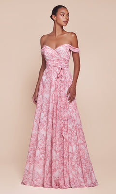 A woman stands against a neutral background wearing the Long Floral-Print A-Line Prom Dress: Ladivine 7441, a floor-length pink gown with off-the-shoulder sleeves, a sweetheart neckline, floral print, and a tied sash at the waist.