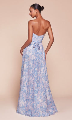 A woman models the Strapless Long Print Prom Dress CL7443, featuring a floor-length blue and pink floral print, sweetheart neckline, and a bow at the fitted back, against a light beige background.