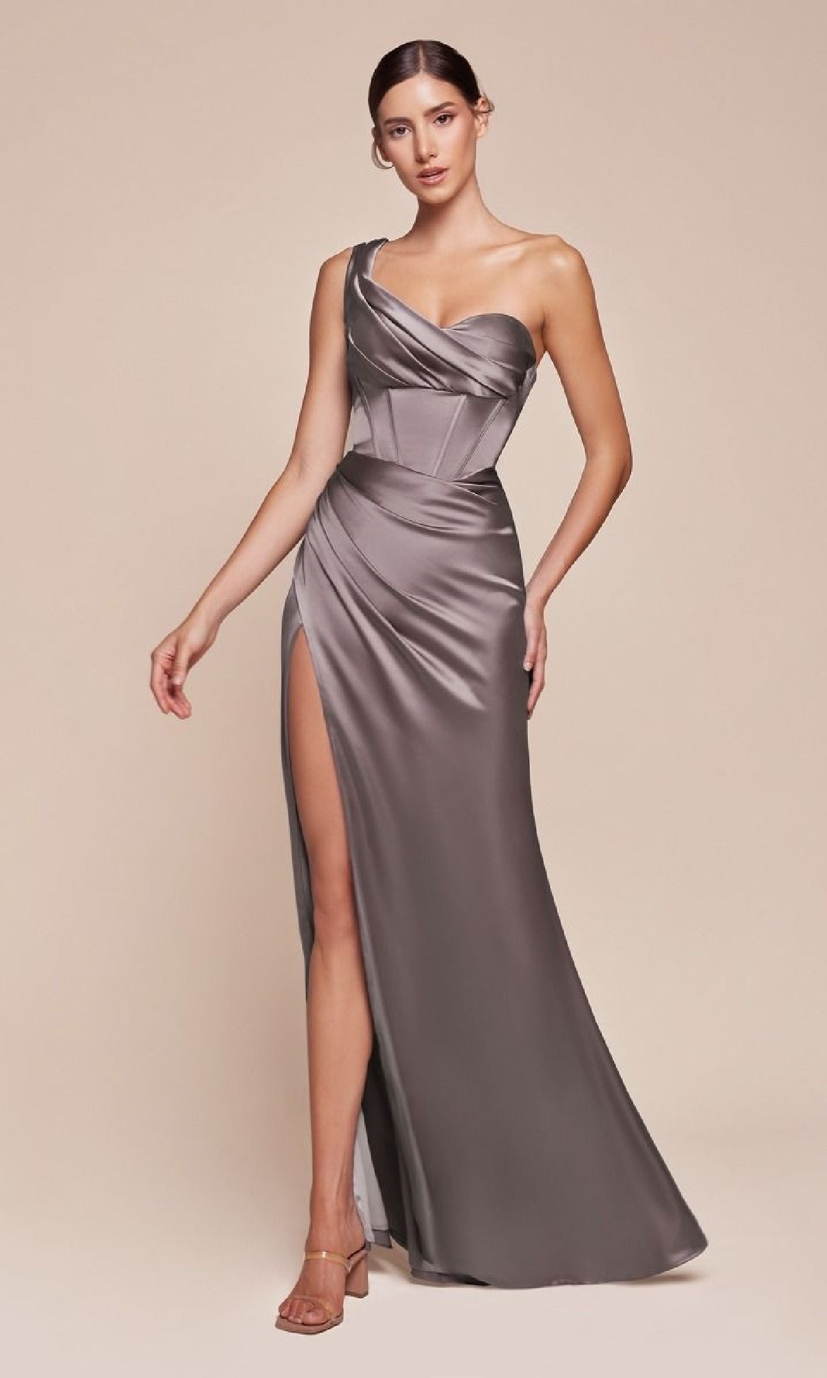 A woman models the Ladivine 7448, a silver one-shoulder lace-up prom dress with a corset bodice and thigh-high slit, against a plain beige background.