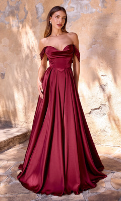 A woman stands before a textured beige wall, wearing the CL7449 Lace-Up Long Satin Prom Dress—an off-the-shoulder, floor-length burgundy gown with a full skirt.