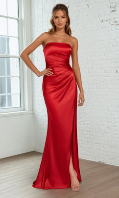 A woman poses by a white brick wall and window, wearing the Ladivine 7451—a simple strapless long prom dress in elegant red satin with a fitted bodice and high slit.