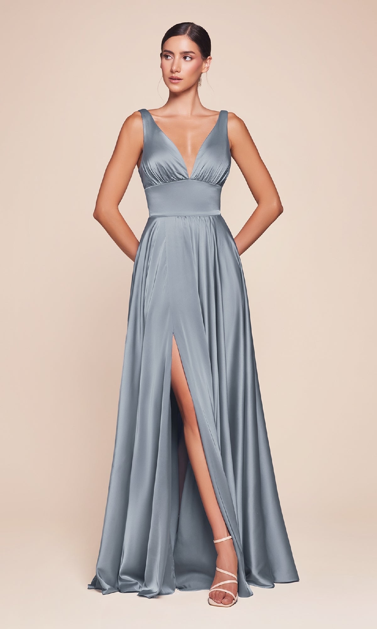 A woman wears the A-Line V-Neck Classic Long Satin Prom Dress in slate blue, featuring a sleeveless design, deep neckline, and high slit, styled with strappy heels against a neutral background.