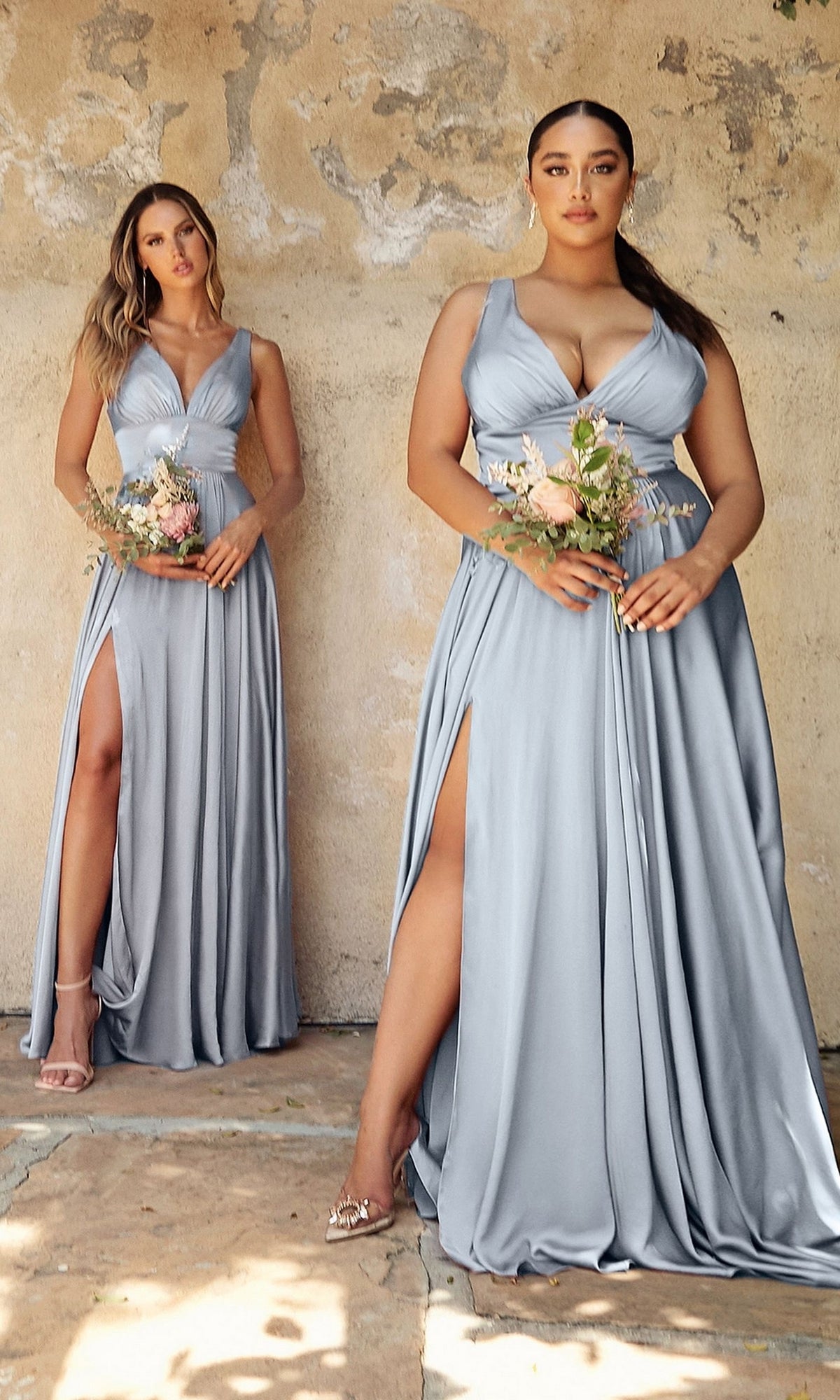 Two women wear A-Line V-Neck Classic Long Satin Prom Dresses with thigh-high slits and hold small floral bouquets, standing against a weathered beige wall.