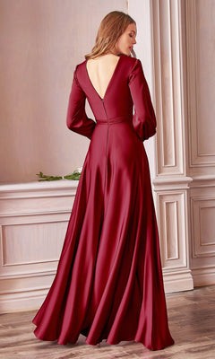A woman stands indoors wearing the Split Long Sleeve Long Formal Dress 7475 in burgundy, its open back and flowing fabric cascading elegantly as she faces away from the camera.