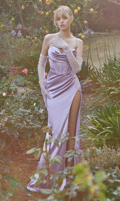 A woman in the Ladivine 7483 Long Satin Prom Dress, featuring a corset-style bodice and high slit, stands in a garden with roses, lemon trees, and greenery, wearing long white gloves.