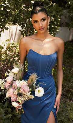 Woman in a Corset Off-the-Shoulder Long Prom Dress 7484 holds a bouquet of flowers, standing outdoors against a lush green backdrop.