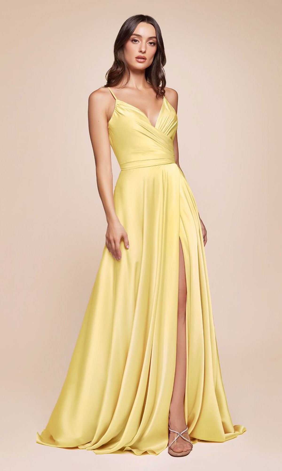 A woman models the Ladivine 7485 Classic Long Satin Formal Prom Dress, a sleeveless yellow gown with a wrap bodice and high slit, against a plain beige background.