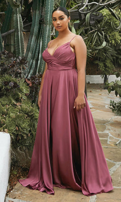 A woman stands outdoors on a stone path, surrounded by green plants and succulents, wearing the Classic Long Satin Formal Prom Dress: Ladivine 7485—a floor-length gown with a fitted bodice and spaghetti straps.