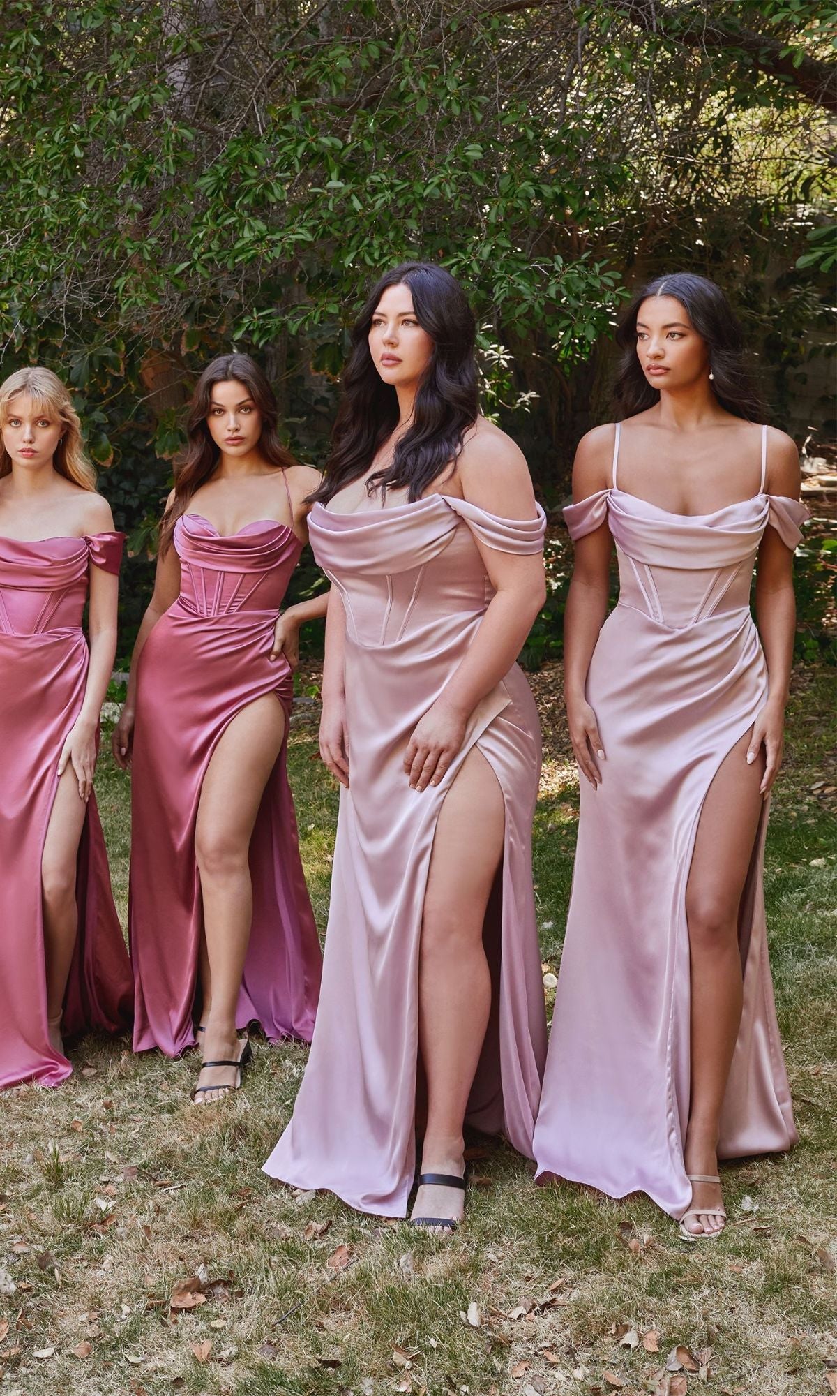 Four women pose outdoors on the grass, wearing Off-the-Shoulder Satin Prom Dress 7492 in light pink and mauve shades, featuring thigh-high slits and a soft satin finish. Trees form a lush backdrop for this elegant scene.