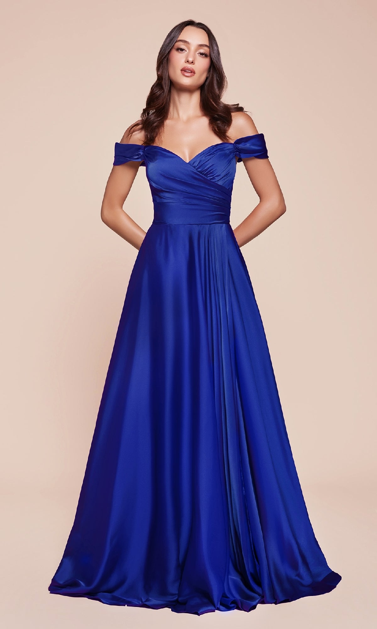 A woman wearing the Empire-Waist Plus-Size Long Prom Dress 7493C, a royal blue, off-the-shoulder satin gown with pockets, stands against a neutral background.