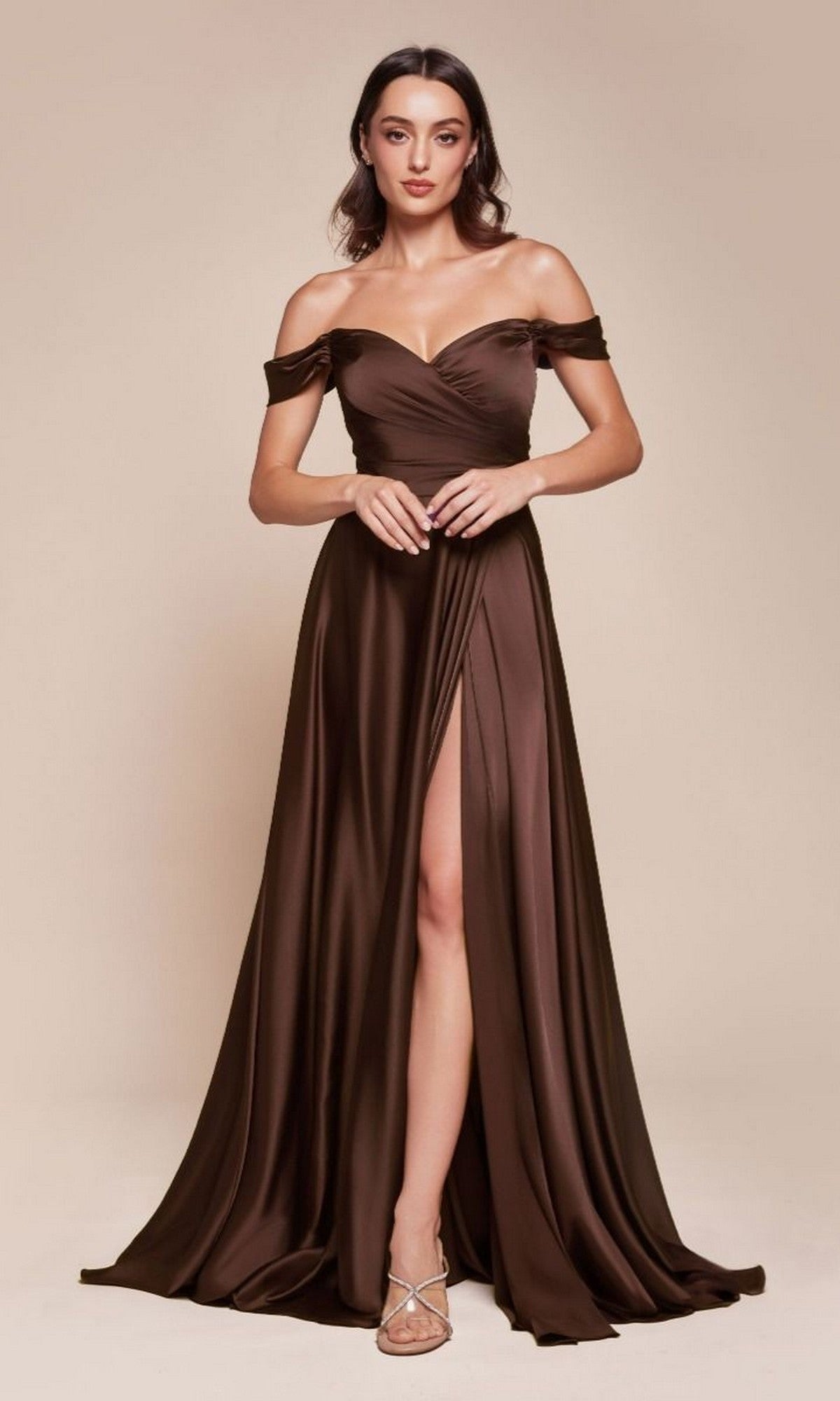 A woman poses in a studio wearing the Classic Off-Shoulder Long A-Line Prom Dress 7493 in Espresso, featuring a floor-length satin silhouette with a high slit, paired with strappy heels.