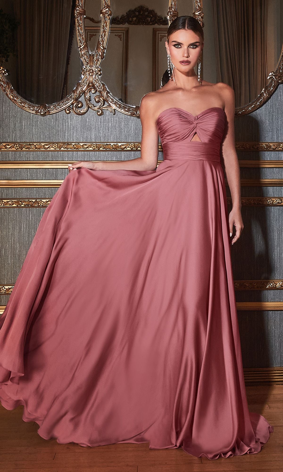 A woman poses indoors in the Strapless Sweetheart Long A-Line Prom Dress 7496, holding out part of the mauve skirt with one hand; ornate decor and a large mirror are in the background.