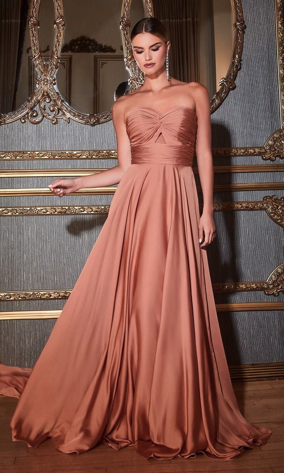 A woman wearing the Strapless Sweetheart Long A-Line Prom Dress 7496 stands in an ornately decorated room with gold-trimmed walls and a large mirror, highlighting the elegance of her floor-length peach formal gown.