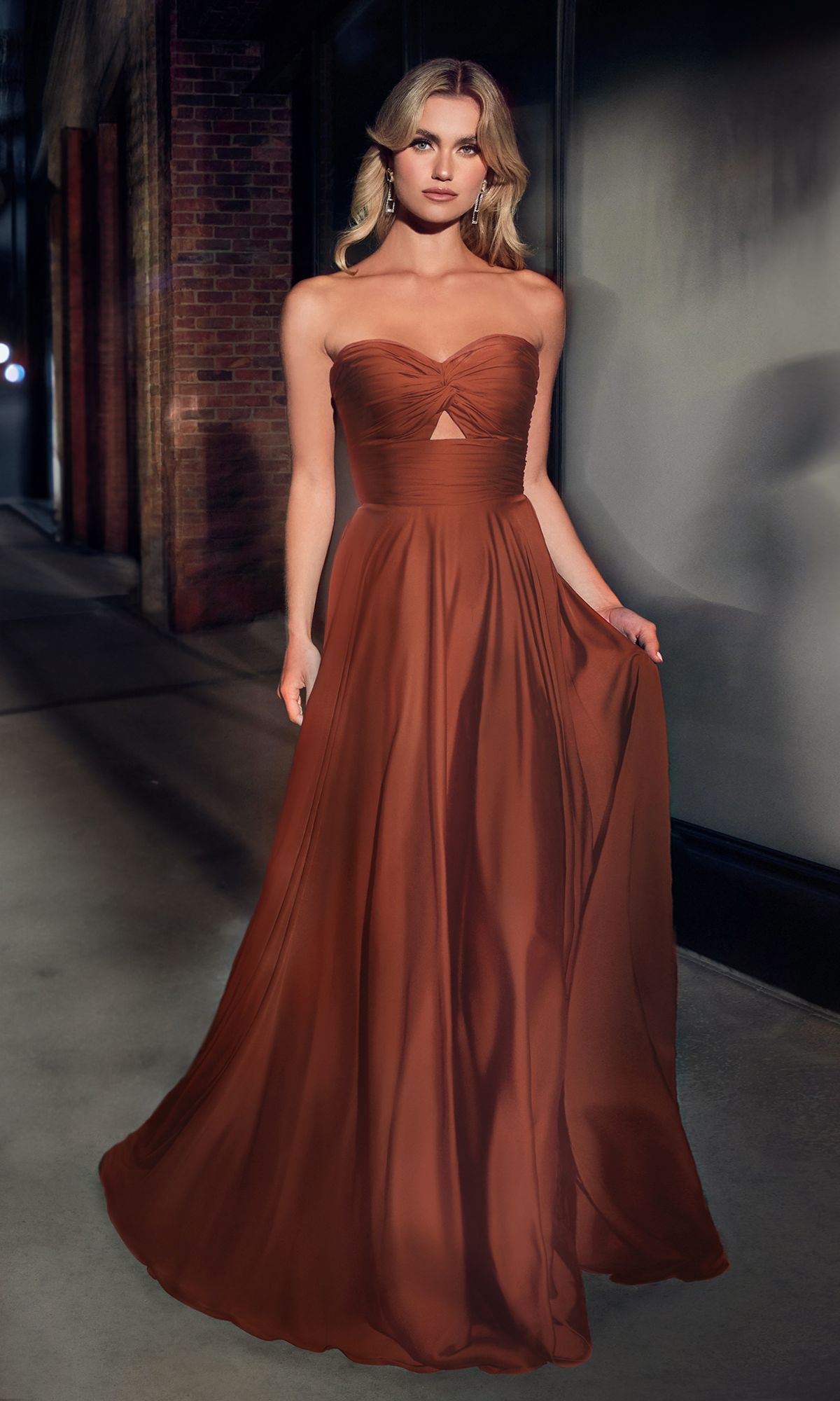 A woman stands on a city sidewalk at night wearing the Strapless Sweetheart Long A-Line Prom Dress 7496, a rust-colored, floor-length gown with a fitted bodice and flowing skirt.