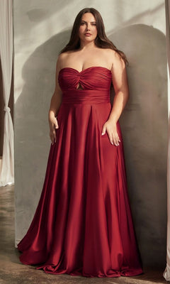 A woman stands against a light wall in the Plus-Size Strapless Sweetheart Prom Dress 7496C—a floor-length red gown with a ruched bodice and small keyhole cutout.