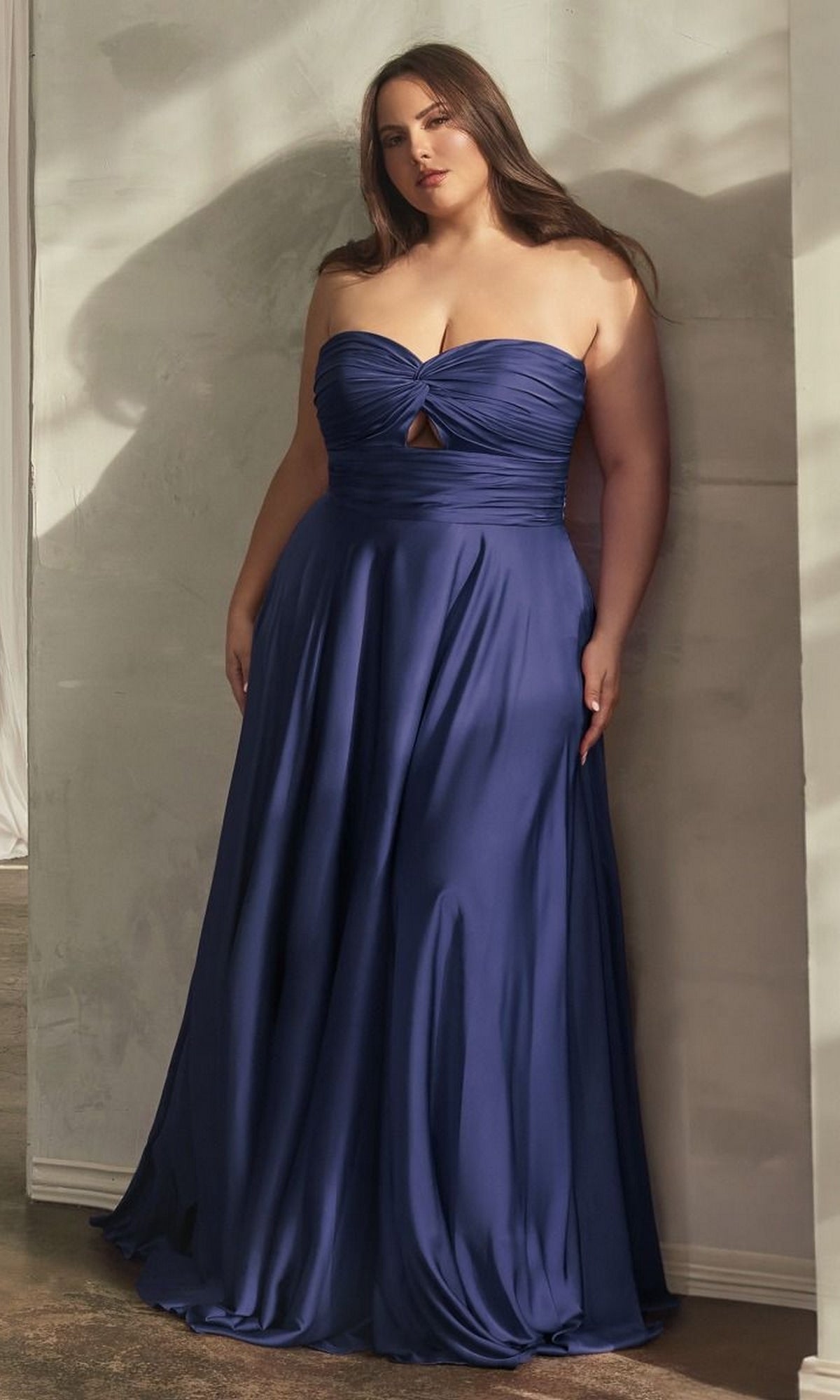 A woman in a strapless sweetheart gown stands against a light wall, wearing the Plus-Size Strapless Sweetheart Prom Dress 7496C in navy—a stunning, floor-length, affordable evening dress perfect for any special occasion.