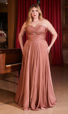 A woman stands indoors in the Plus-Size Strapless Sweetheart Prom Dress 7496C, a rose-colored, floor-length gown with a gathered bodice and side pockets. A piano and red curtains are in the background. This elegant gown is an affordable evening dress choice.