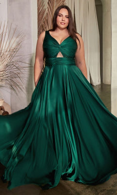 A woman stands indoors near decorative plants wearing the Twist-Front Long Plus-Size Prom Dress 7497C, a sleeveless dark green satin formal gown with a flowing skirt and front cutout.