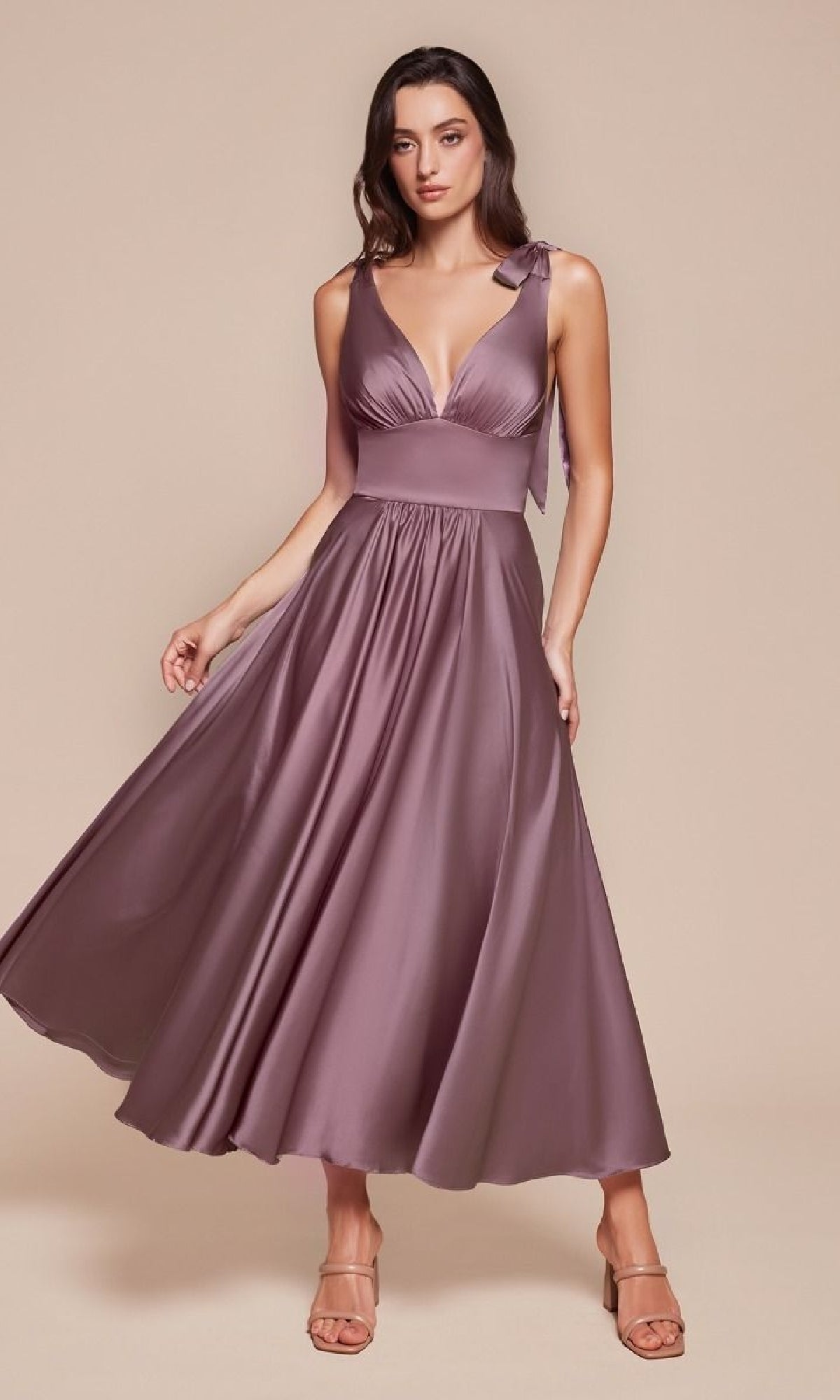 Woman wearing the Ladivine 7499 Tea-Length Wedding-Guest Dress, a sleeveless mauve satin A-line midi with fitted waist and flared skirt, posing against a plain beige background.