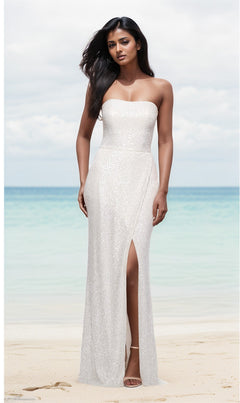 A woman stands on a sandy beach in the white La Femme Strapless Long Sequin Prom Dress 29681, featuring a thigh-high slit and shimmering sequins that catch the light with the ocean in the background.