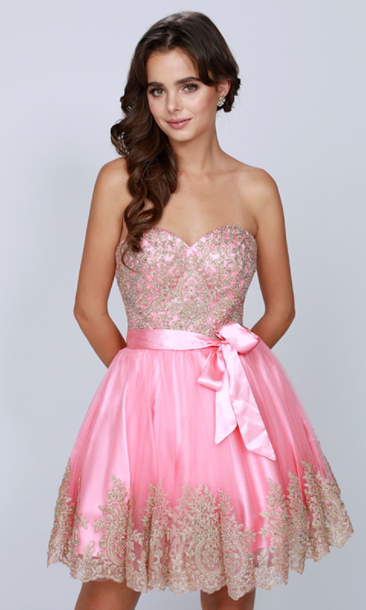 A woman models the Short Hoco Dress: Juliet 759, a strapless homecoming dress with gold embroidery, a waist bow, and an elegant lace-up back, set against a plain light background.