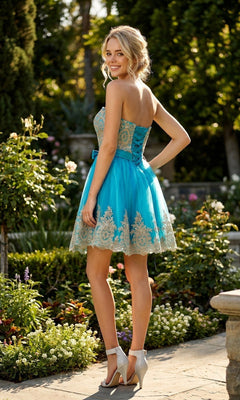 A woman wears the Juliet 759 Short Hoco Dress, featuring a strapless fit-and-flare design with blue and gold lace, standing outdoors in a garden and smiling over her shoulder, her high heels adding elegance to the look.