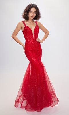 A woman wears the Nina Canacci 7600 Lace Mermaid Prom Dress, a sleeveless, form-fitting red gown with a deep V neckline and sparkling embellishments, standing against a plain light background.
